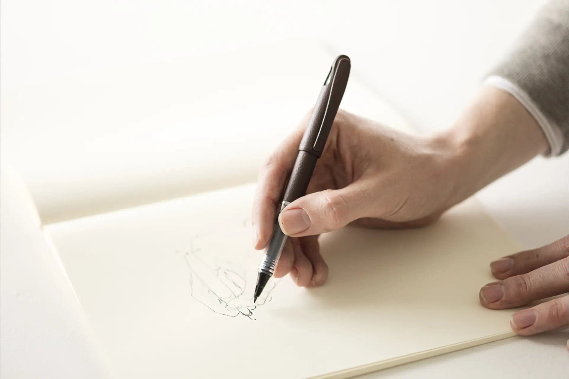 Hand writing with a pen in an open Midori MD Notebook lying flat on a white desk