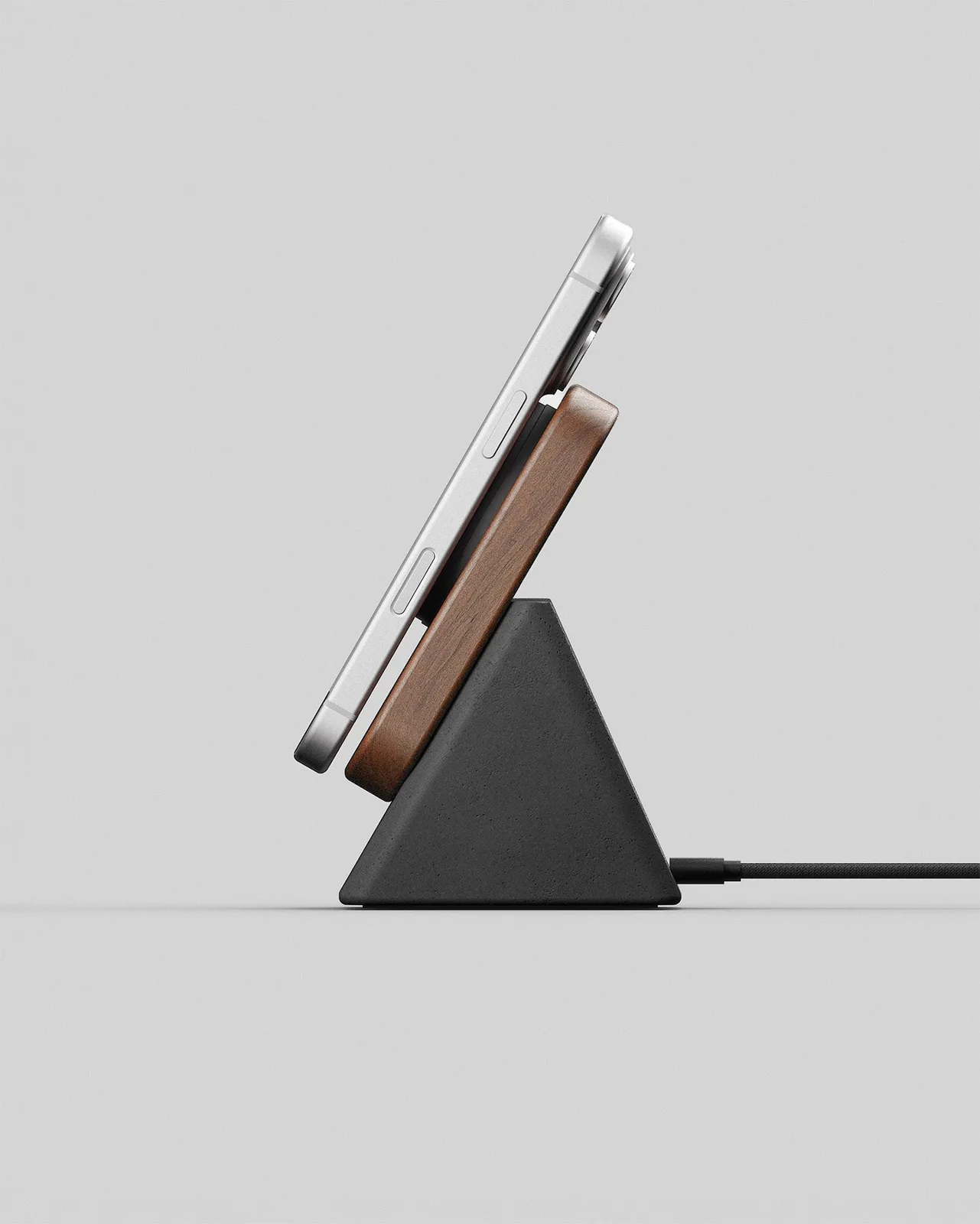 Side view of the Modhaus Upright wireless charging stand with a solid walnut top on a charcoal concrete base holding an iPhone