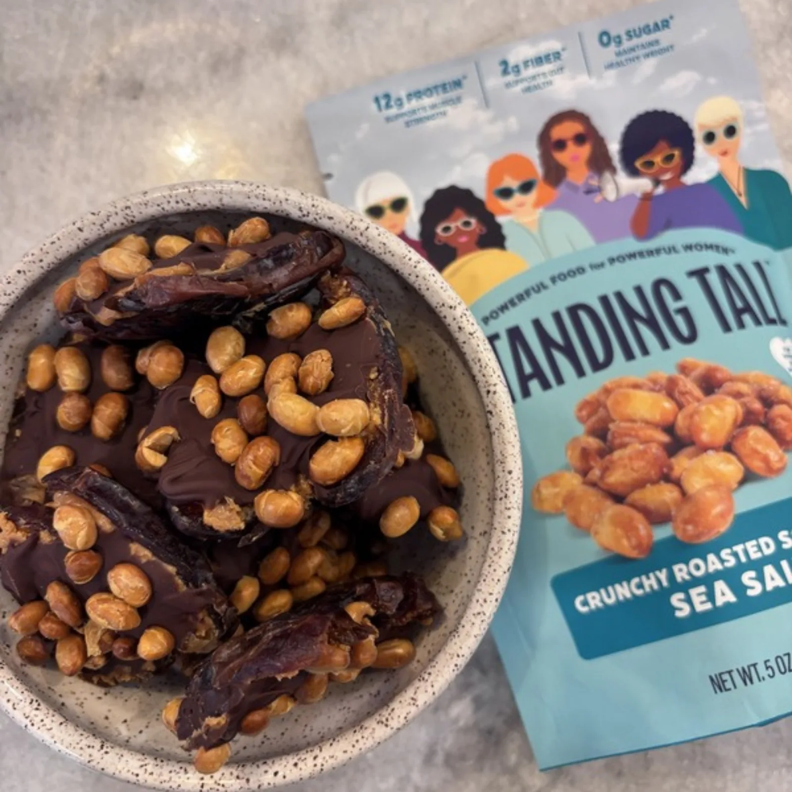 Bowl of chocolate-covered dates topped with Standing Tall roasted soybeans next to a bag of Standing Tall Sea Salt Crunchy Roasted Soybeans