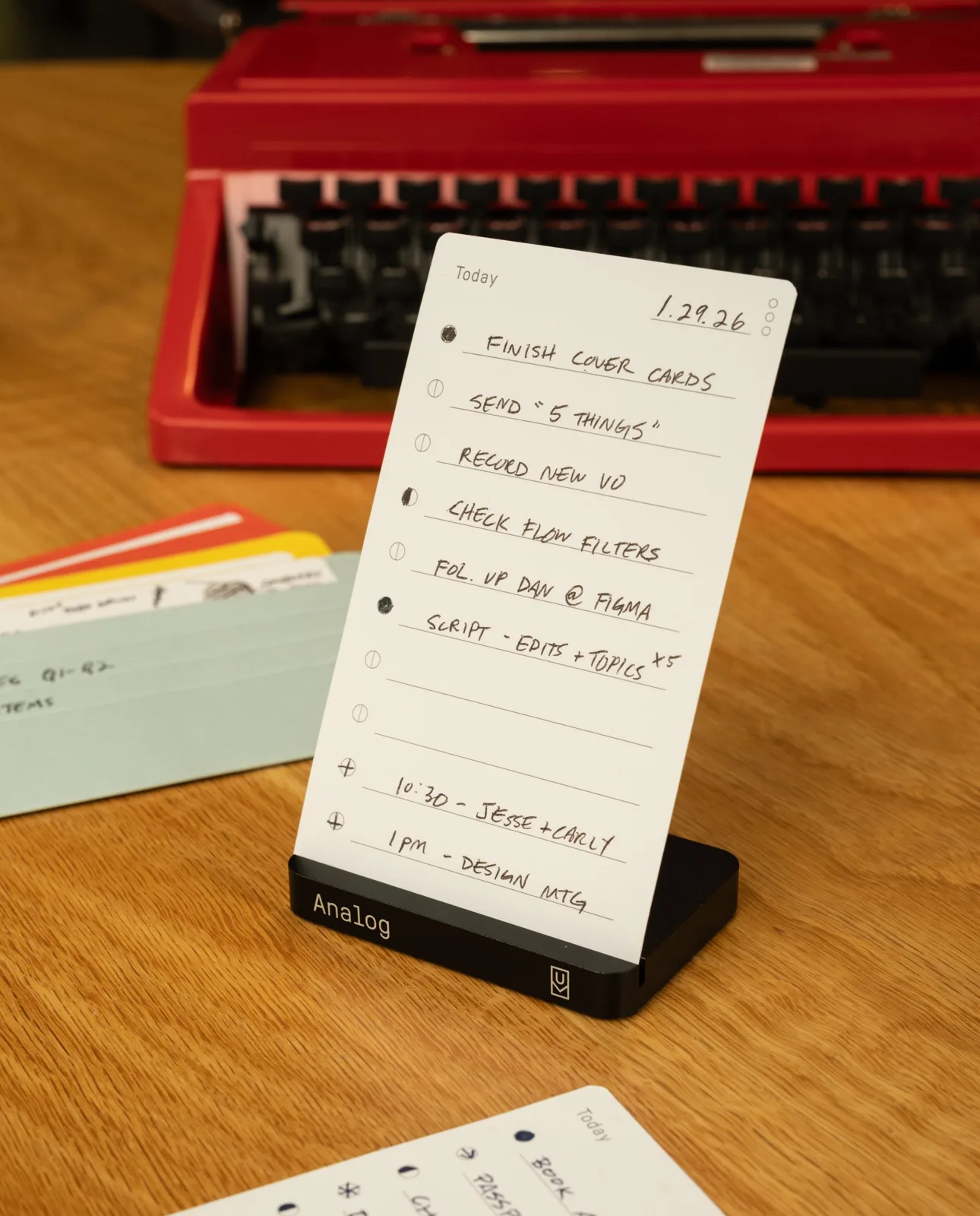 Ugmonk Analog Today card standing in a black aluminum holder beside a red typewriter on a wood desk